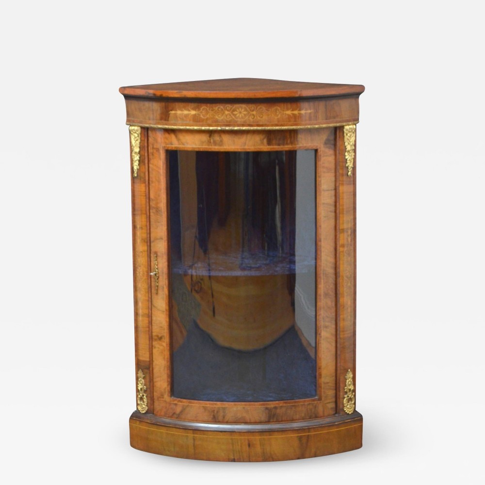 A nineteenth-century Victorian burr walnut corner cabinet featuring floral marquetry inlay, gilt ormolu corner mounts, and a single glazed door.