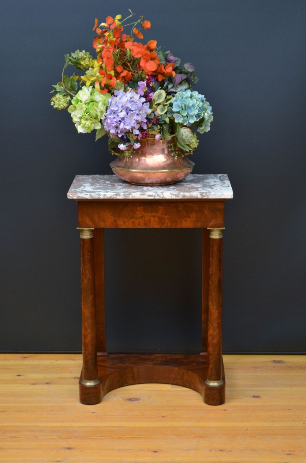 An antique French Empire style mahogany console table featuring a grey and white veined marble top, cylindrical columns with brass mounts, and a curved base plinth.