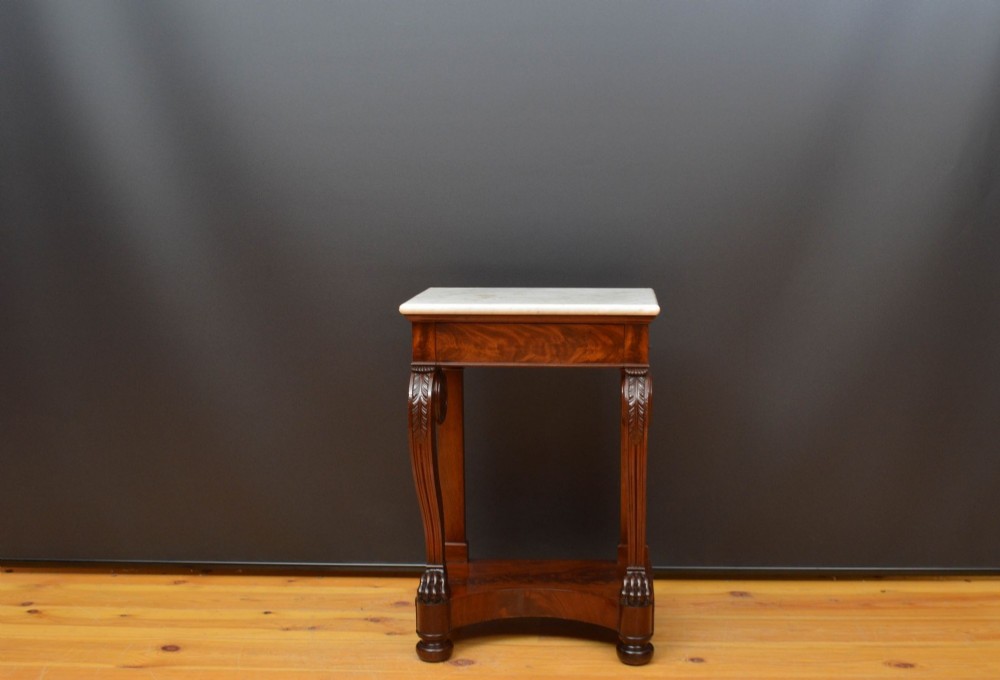 An antique mahogany console table featuring a rectangular white marble top supported by carved scrolling front legs and a plinth base.