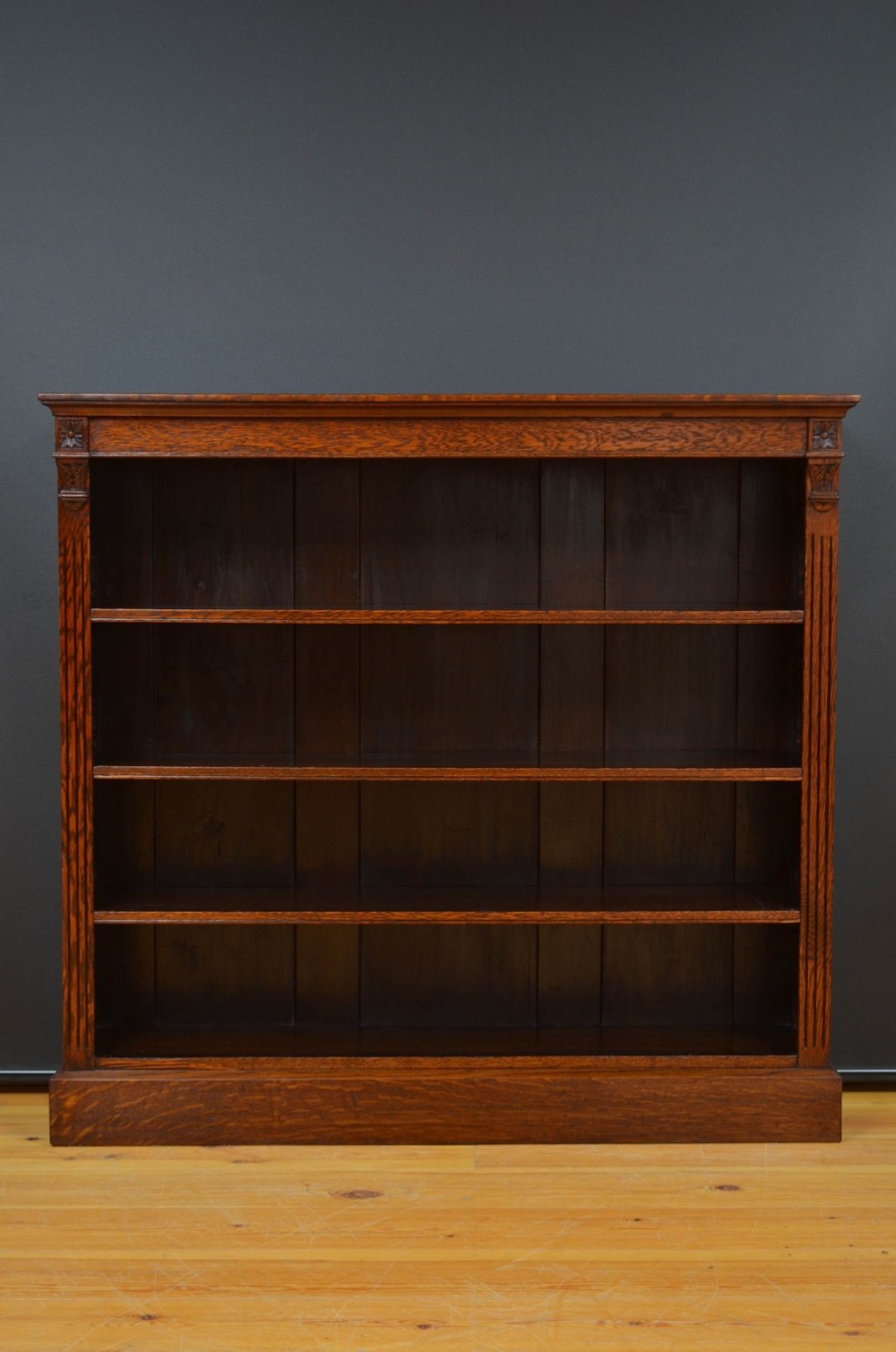 A nineteenth-century dark oak open bookcase featuring four horizontal shelves, fluted side pilasters, and carved rosette details at the top corners.
