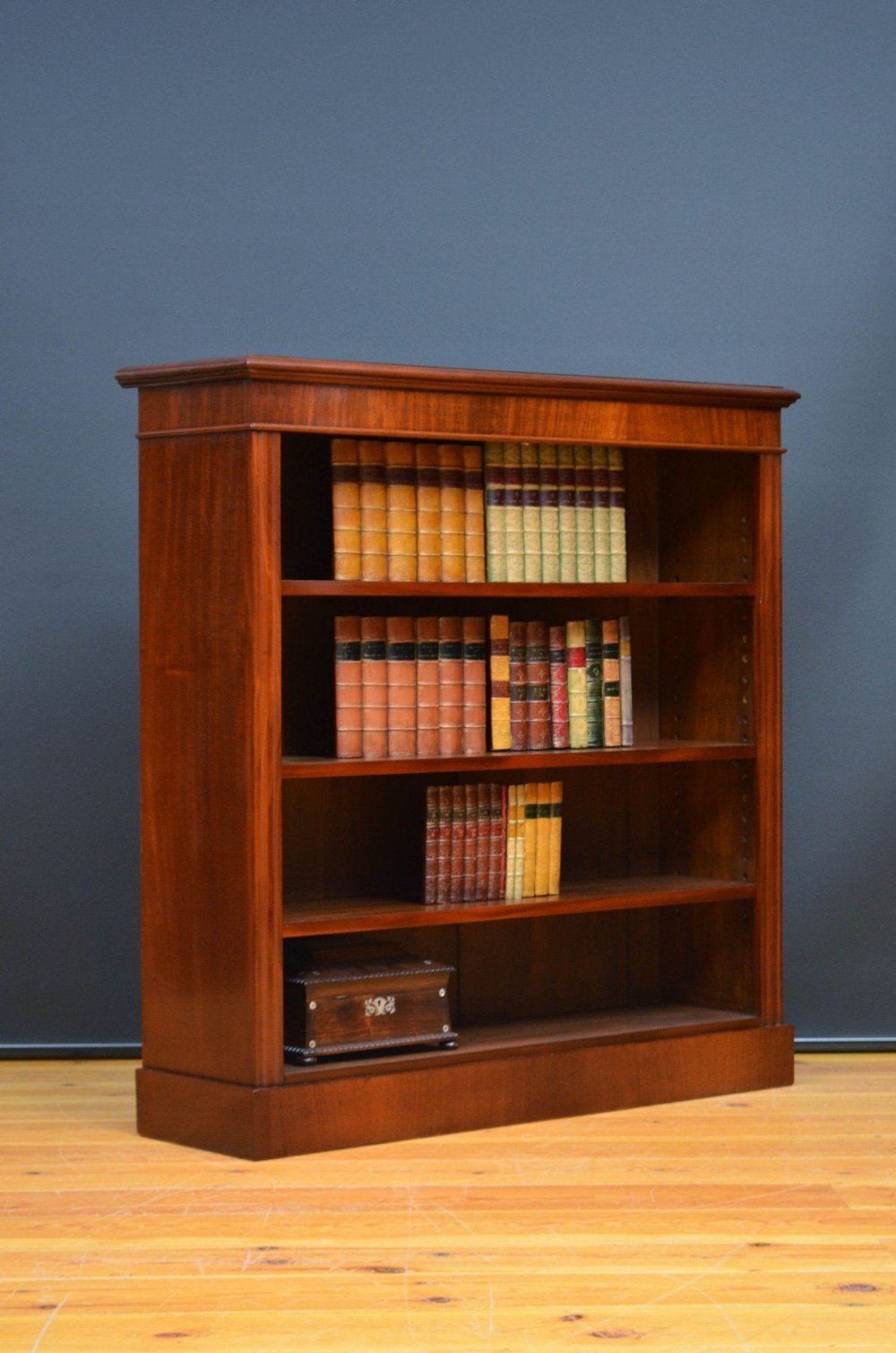 A late Victorian open bookcase crafted in warm walnut timber, featuring three adjustable shelves, a moulded cornice top, and a solid plinth base.