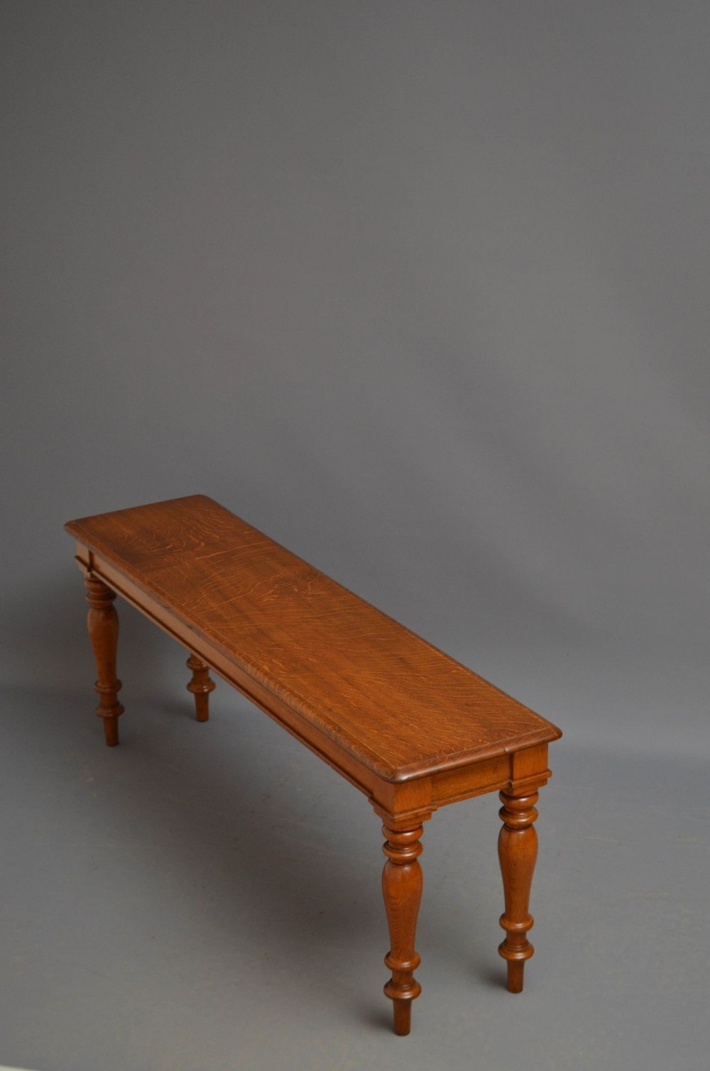 A long Victorian solid oak hall bench featuring a flat rectangular seat and four turned wooden legs.