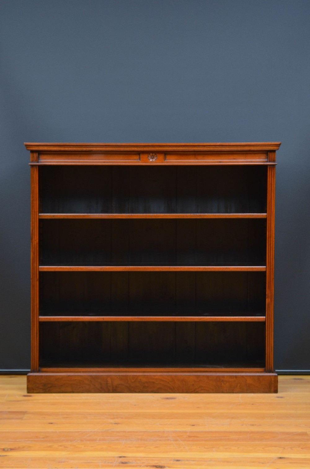 A Victorian solid walnut open bookcase featuring fluted side columns, a central carved rosette medallion on the upper frieze, and four open shelves on a plinth base.