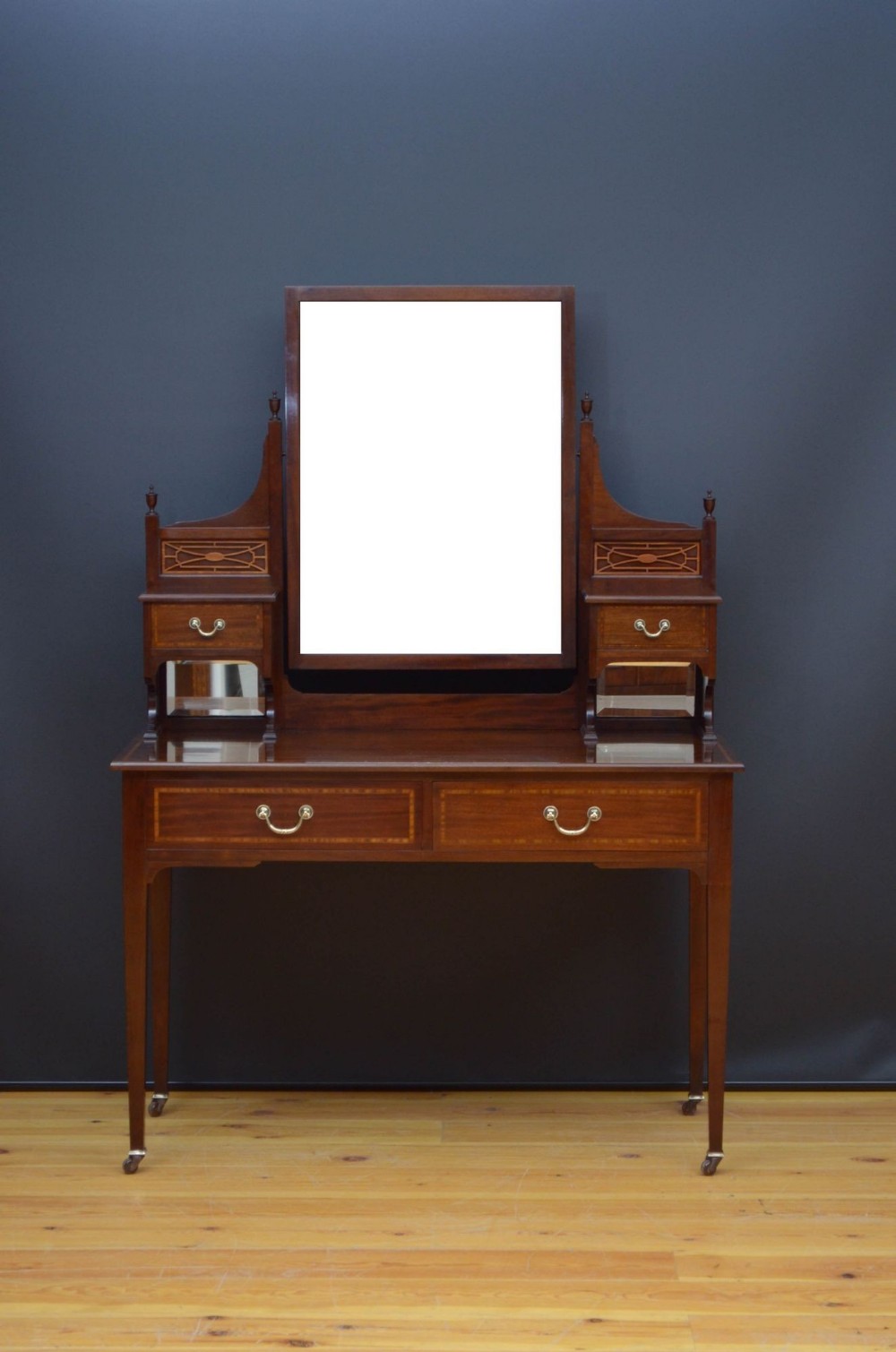 An Edwardian mahogany dressing table featuring a central rectangular mirror, side trinket drawers with fretwork panels, two main frieze drawers with brass handles, and square tapered legs on castors.
