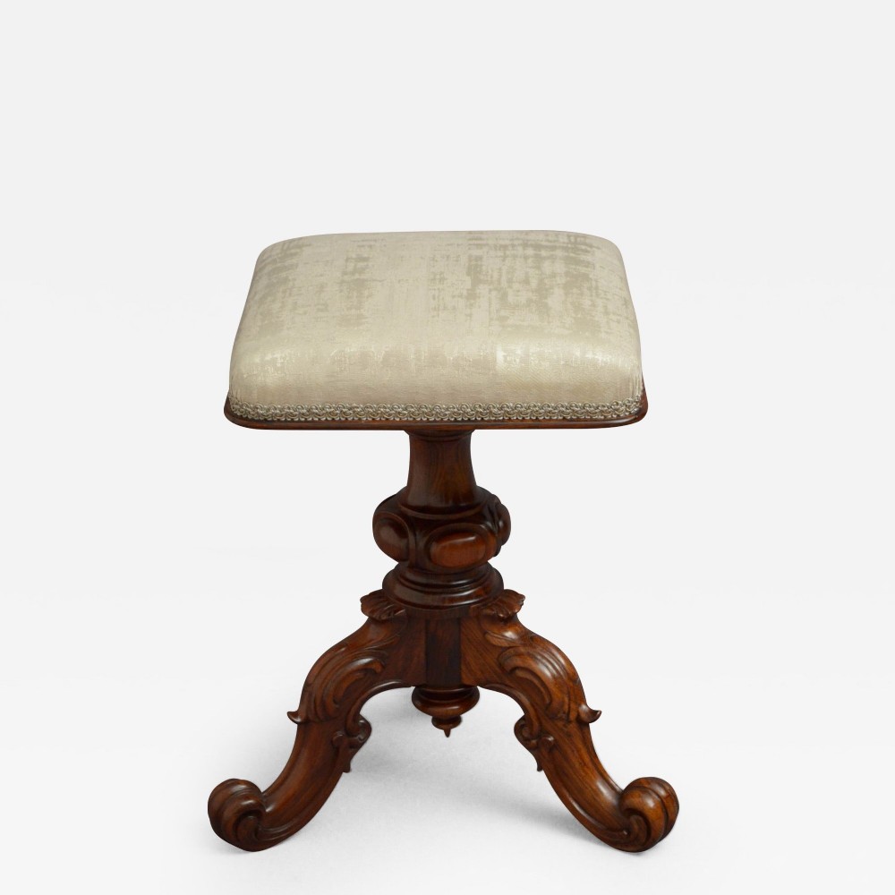 A Victorian rosewood height-adjustable stool featuring a square cream-upholstered seat with braided trim, set upon a turned central column with carved tripod scrolled legs.