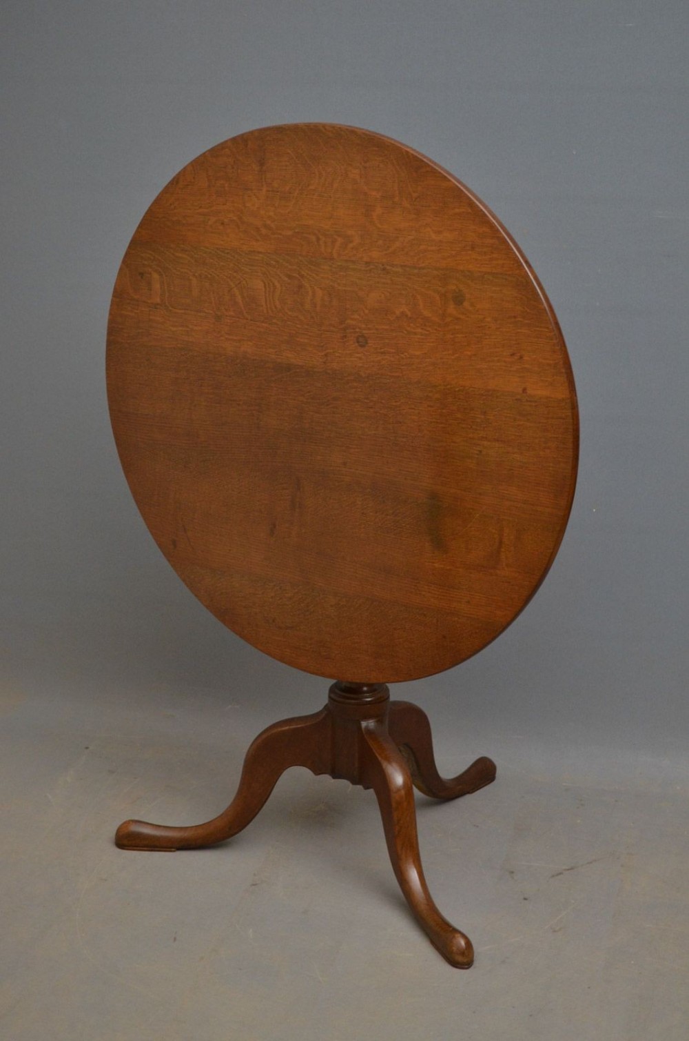 A Georgian period circular oak tilt-top table shown with the top fixed in a vertical position resting on a turned tripod pedestal.