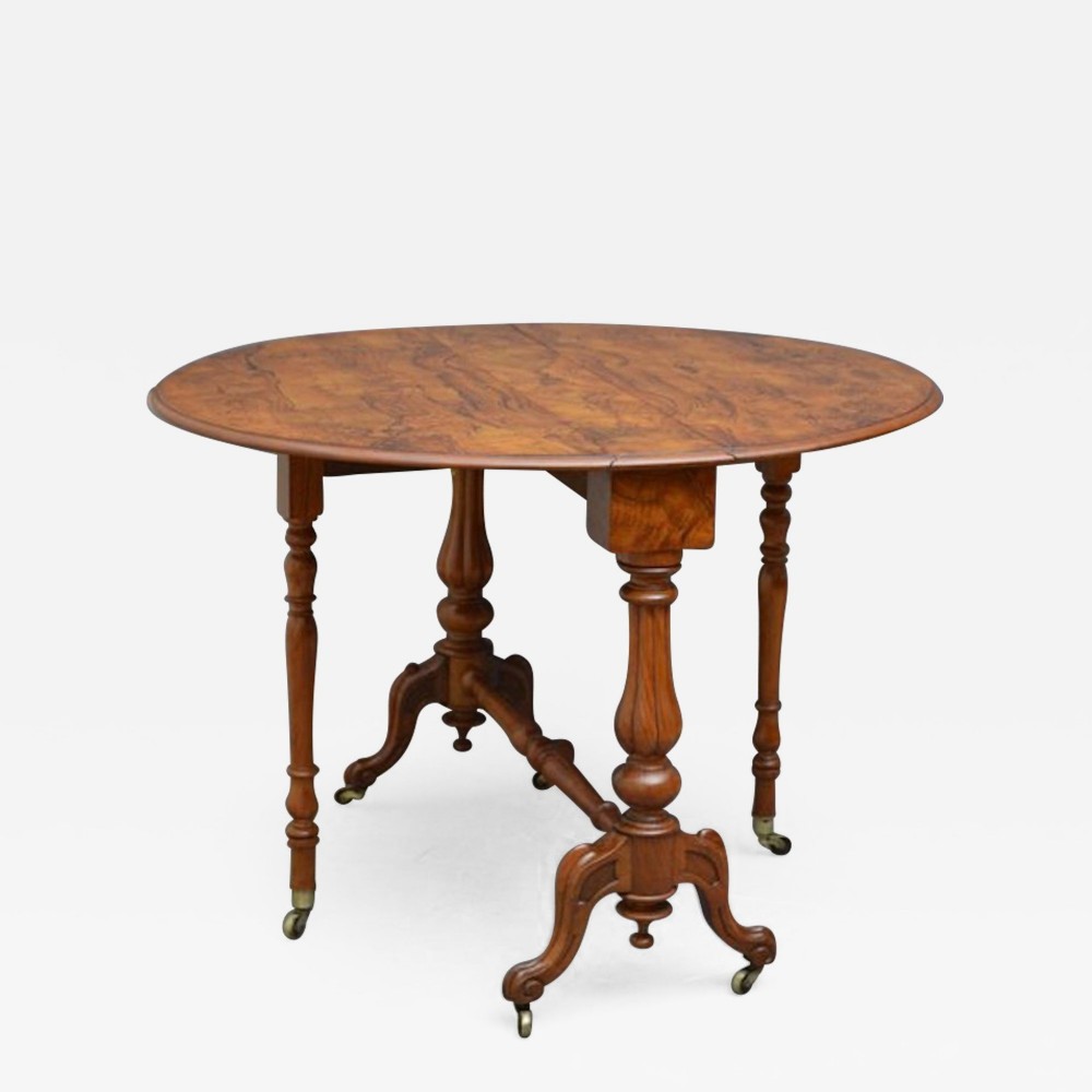 A Victorian walnut Sutherland table with a drop-leaf top, turned dual-column supports, carved legs, and brass castors.