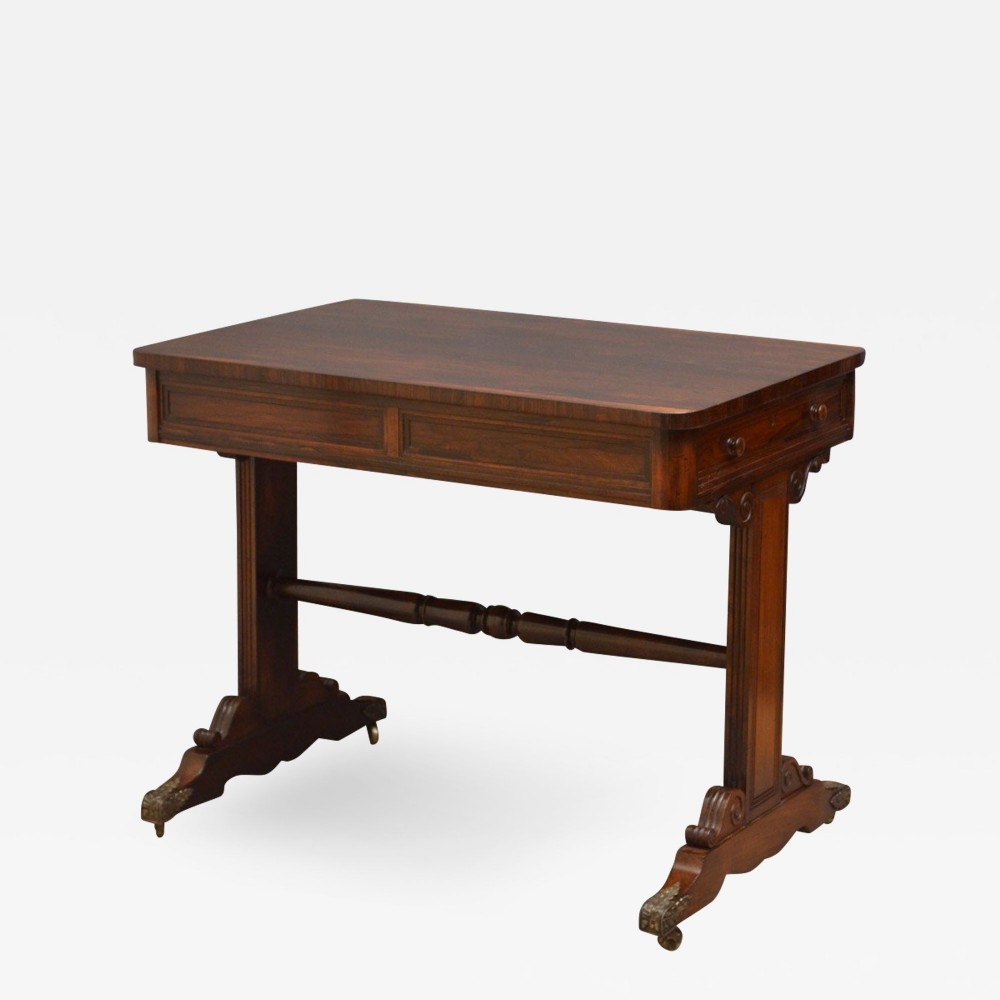 A small Regency rosewood library table with end-standard supports, scrolled feet, a turned central stretcher, and brass castors.