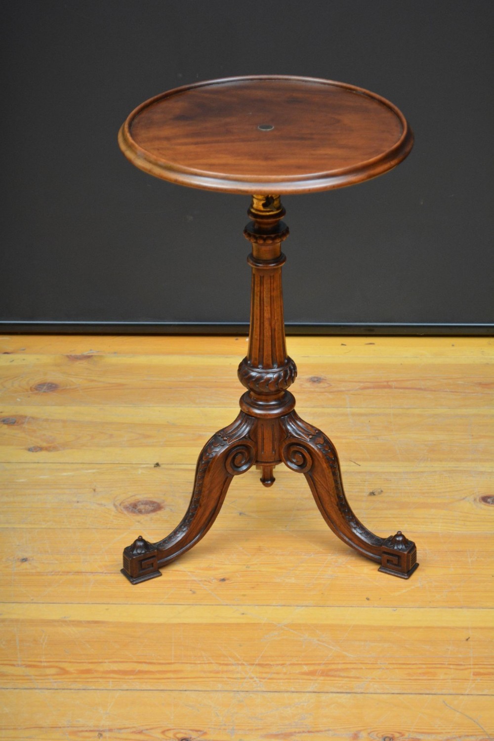 A Victorian dark mahogany height-adjustable side table featuring a circular dished top, fluted central column, and a carved tripod base.