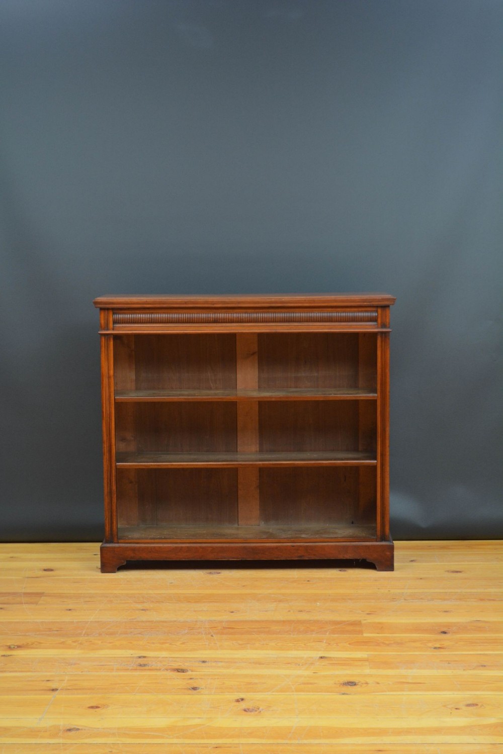A Late Victorian open walnut bookcase featuring three horizontal shelves, reeded frieze detailing, and a plinth base.