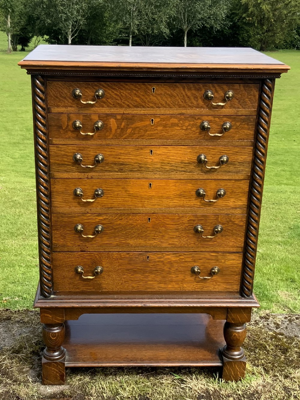 A late Victorian oak tall chest featuring six drawers flanked by barley twist columns resting on turned legs with a open bottom shelf.
