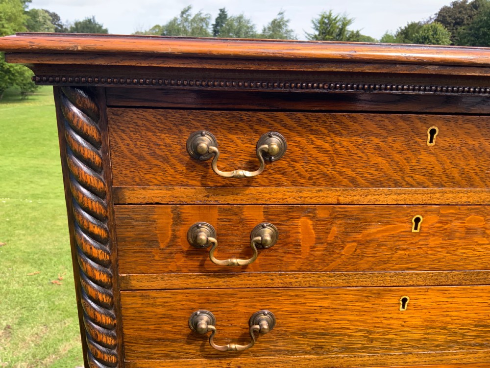 A late Victorian oak tall chest featuring six drawers flanked by barley twist columns resting on turned legs with a open bottom shelf. View II