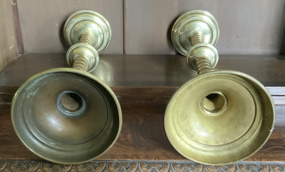 A pair of tall Victorian Gothic Revival brass candlesticks featuring barley twist columns, central knops, crenellated top drip pans, and circular stepped bases. View IV