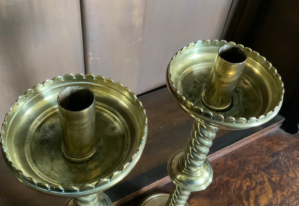 A pair of tall Victorian Gothic Revival brass candlesticks featuring barley twist columns, central knops, crenellated top drip pans, and circular stepped bases. View V