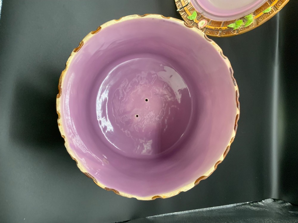A Victorian George Jones majolica cheese keep featuring a wooden stave texture, moulded green leaves, pink flowers, and a twisted vine handle, alongside a matching base plate with a lilac interior glaze. View IV