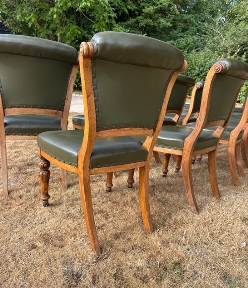 A set of fourteen Victorian oak dining chairs upholstered in dark green leather with turned front legs resting on castors. View II