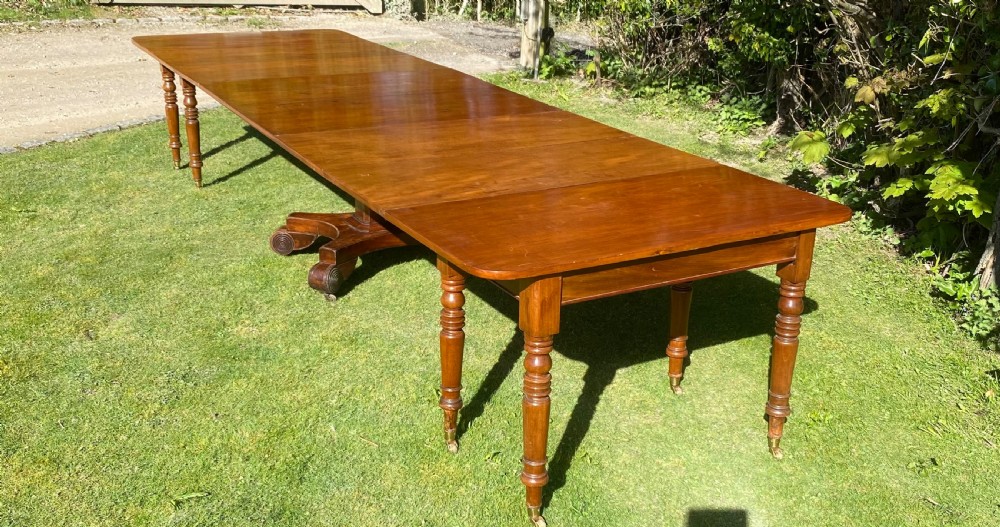 An exceptionally long Early Victorian mahogany extending dining table with turned legs, central pedestal base on scroll feet, and brass castors. View IV