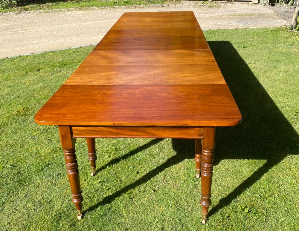 An exceptionally long Early Victorian mahogany extending dining table with turned legs, central pedestal base on scroll feet, and brass castors. View V