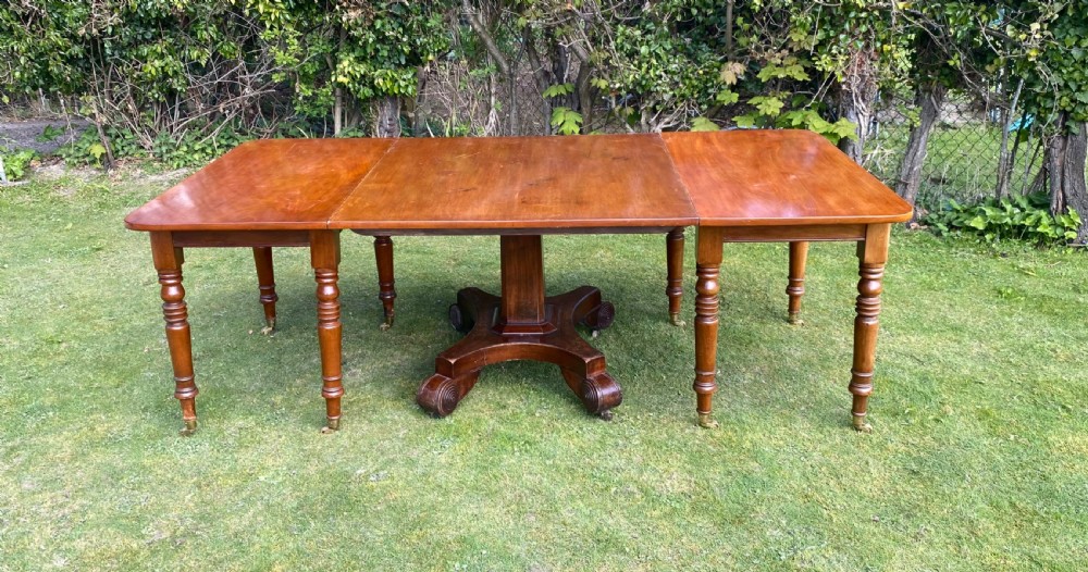 An exceptionally long Early Victorian mahogany extending dining table with turned legs, central pedestal base on scroll feet, and brass castors. View VII