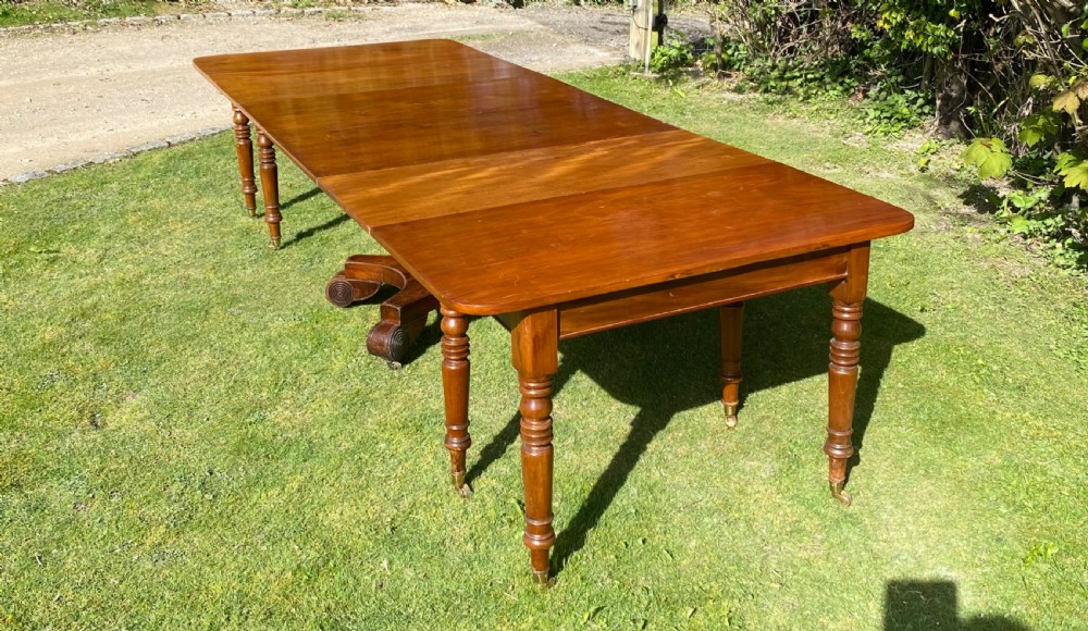 An exceptionally long Early Victorian mahogany extending dining table with turned legs, central pedestal base on scroll feet, and brass castors. View VIII