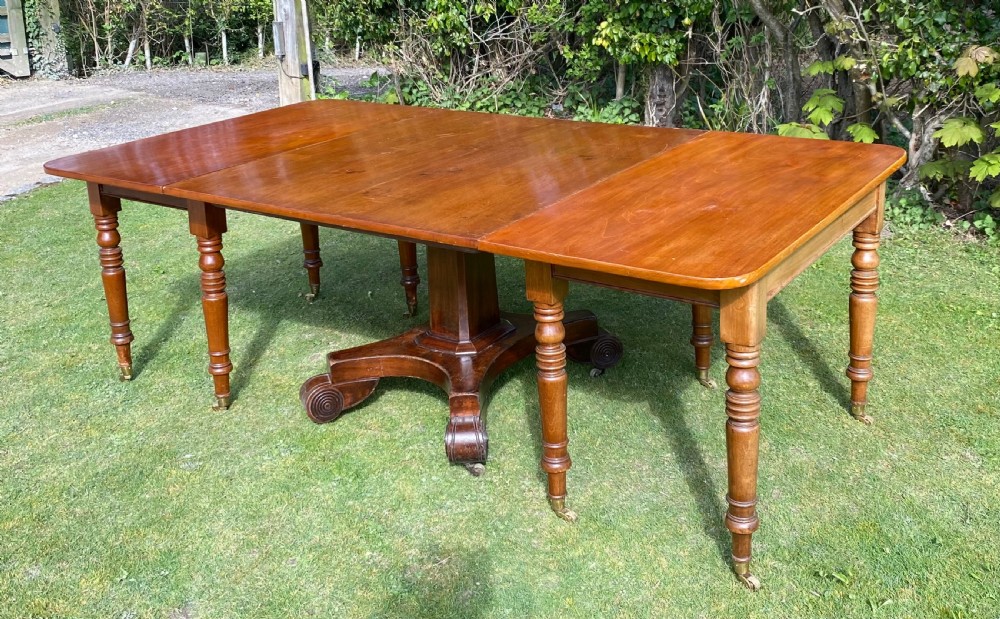 An exceptionally long Early Victorian mahogany extending dining table with turned legs, central pedestal base on scroll feet, and brass castors. View XI