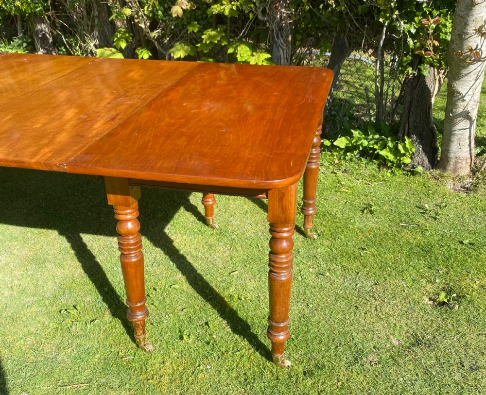 An exceptionally long Early Victorian mahogany extending dining table with turned legs, central pedestal base on scroll feet, and brass castors. View XII
