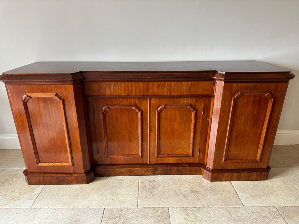 A nineteenth-century Victorian mahogany breakfront sideboard featuring four moulded panel doors and a polished wooden top.
