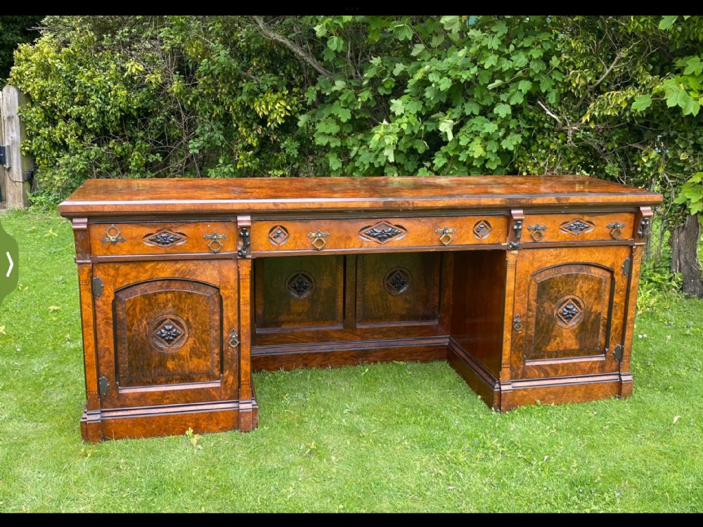 A Victorian carved oak pedestal sideboard featuring burr veneer door panels, carved diamond motifs, multiple top drawers with brass handles, and a central kneehole recess.