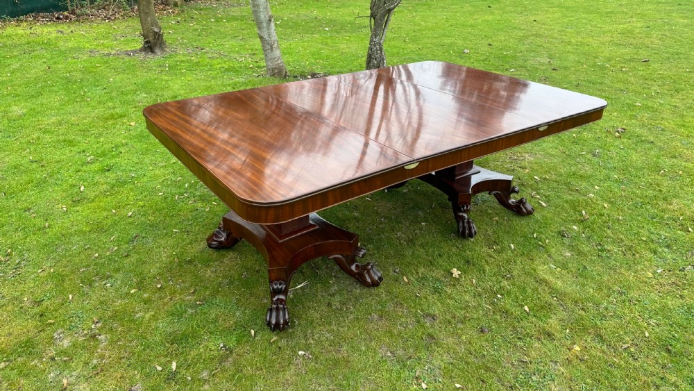 A Regency mahogany twin-pillar extending dining table featuring a polished rectangular top with rounded corners and carved claw-foot pedestal bases.