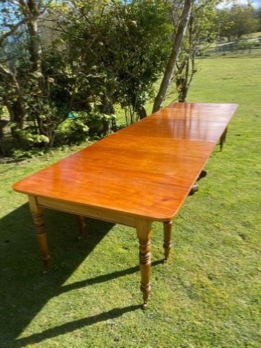 An exceptionally long Early Victorian mahogany extending dining table with turned legs, central pedestal base on scroll feet, and brass castors. View II
