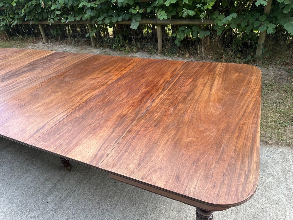 A long mahogany extending dining table with turned fluted legs and brass castors. View II