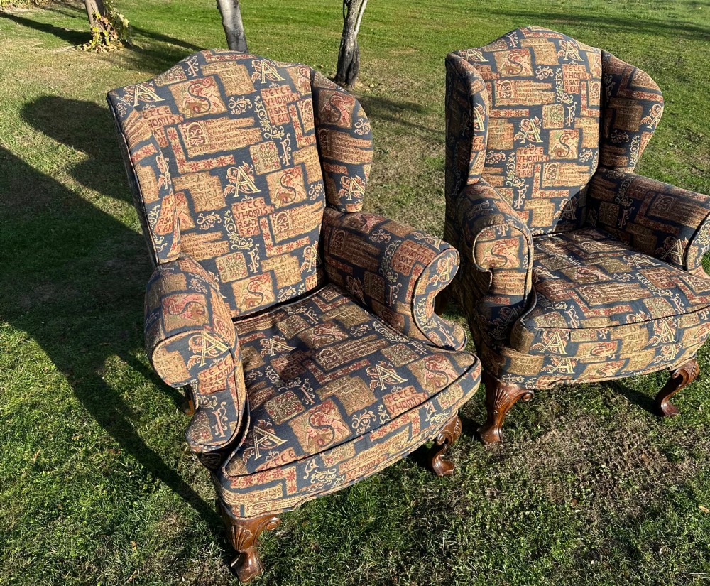 A pair of 1920s wingback armchairs upholstered in a gold and blue manuscript patterned tapestry fabric with carved wooden cabriole front legs. View V