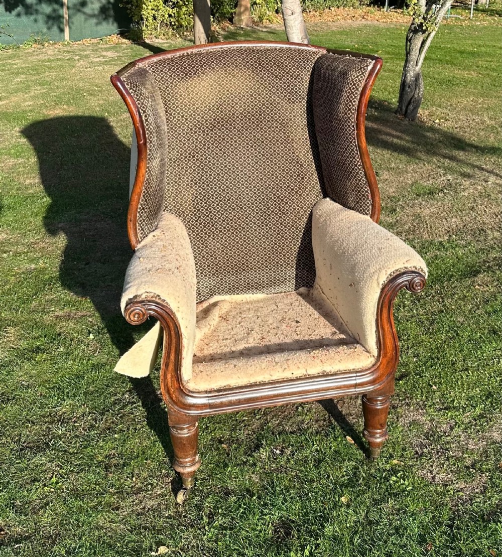 A William IV mahogany wingback armchair featuring patterned fabric on the backrest, scrolled arms, and turned front legs on brass castors.