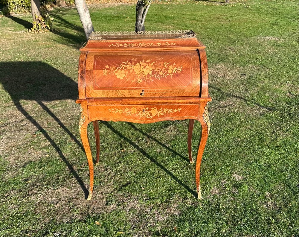 A 19th-century French cylinder roll-top desk crafted with floral marquetry inlays, slender cabriole legs, and brass ormolu mounts.