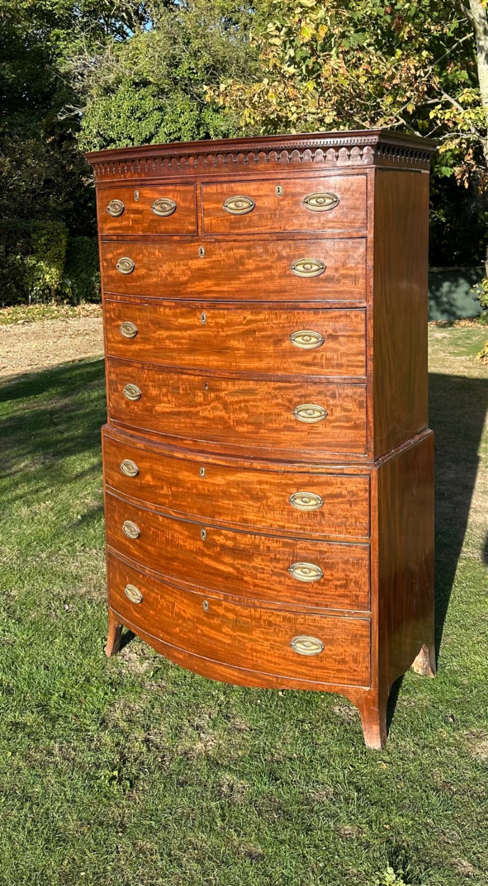 A George III bowfront mahogany chest on chest featuring a decorative top cornice, oval brass handles, and two upper and five lower drawers.
