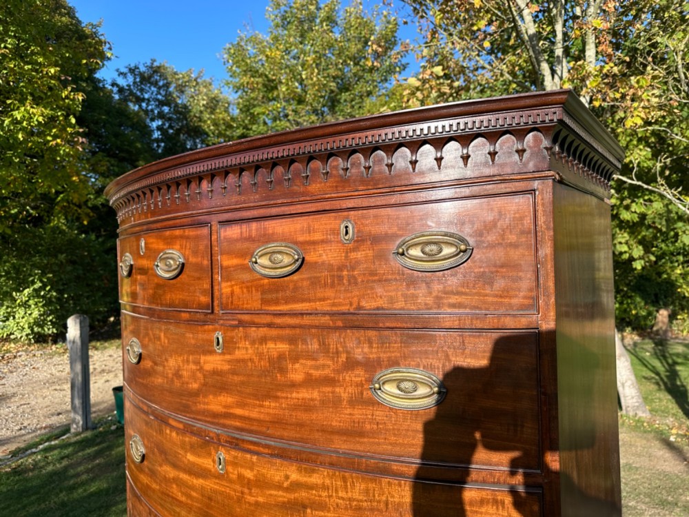 A George III bowfront mahogany chest on chest featuring a decorative top cornice, oval brass handles, and two upper and five lower drawers. View II