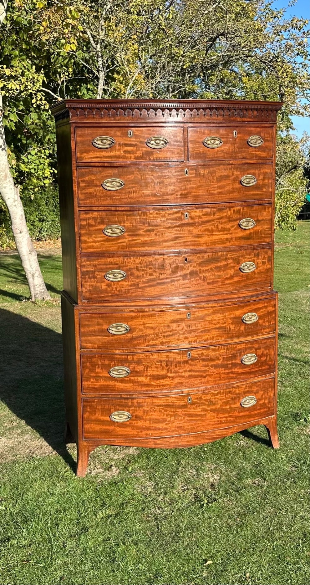 A George III bowfront mahogany chest on chest featuring a decorative top cornice, oval brass handles, and two upper and five lower drawers. View IV
