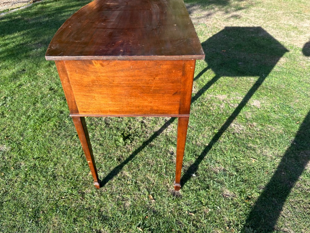 A circa 1920 mahogany bow front side table featuring three drawers with brass oval drop handles and slender tapered legs. View III