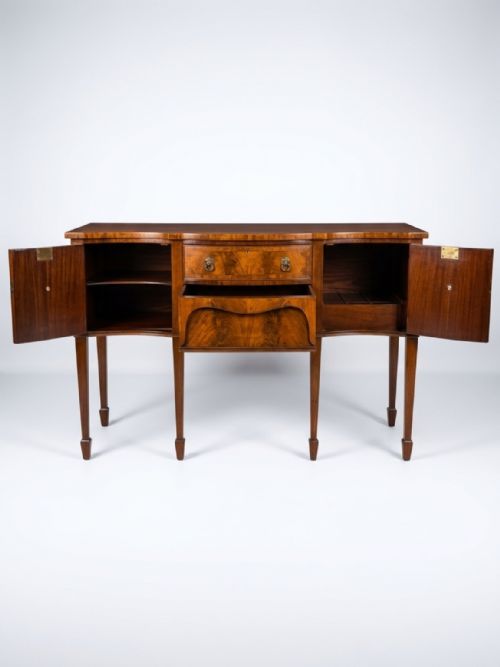 fig 1. A Georgian serpentine-front mahogany sideboard with flame mahogany veneered doors, square tapered legs, and brass lion-mask drop ring handles.