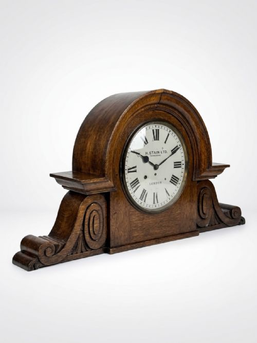 fig 1. An antique carved oak mantel clock featuring an arched top, side scrollwork detailing, and a cream dial with Roman numerals marked H. Stain Ltd. Jewellers London.