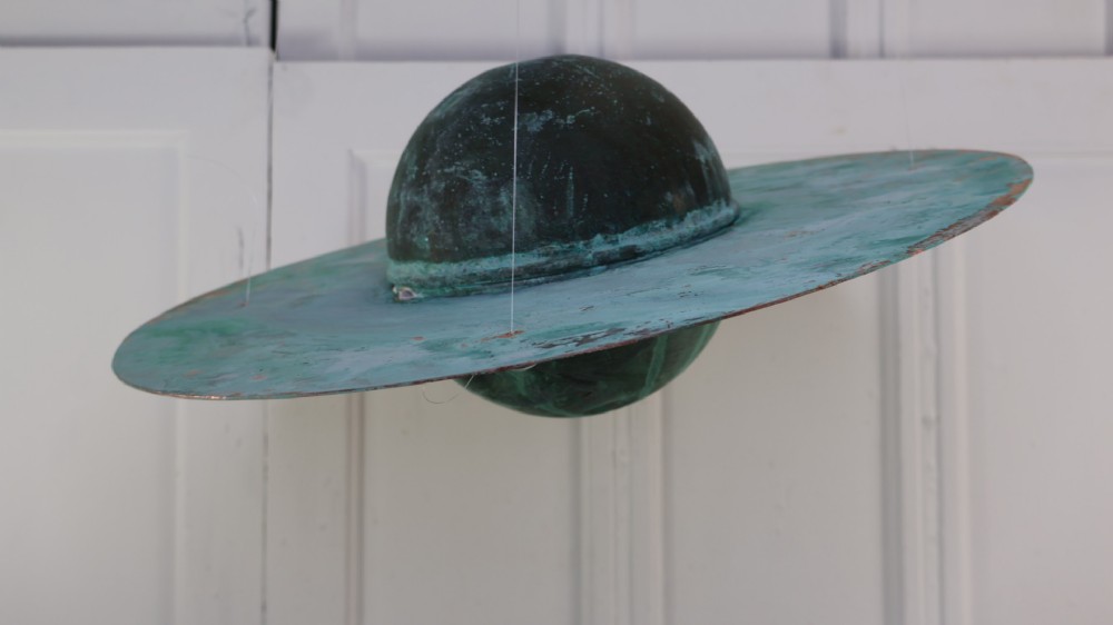 A suspended copper model representing the planet Saturn with a rich verdigris green patina across its central sphere and outer ring.