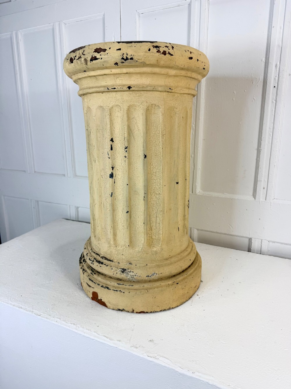A nineteenth-century fluted terracotta display column with a distressed cream painted finish and a circular capital and base.