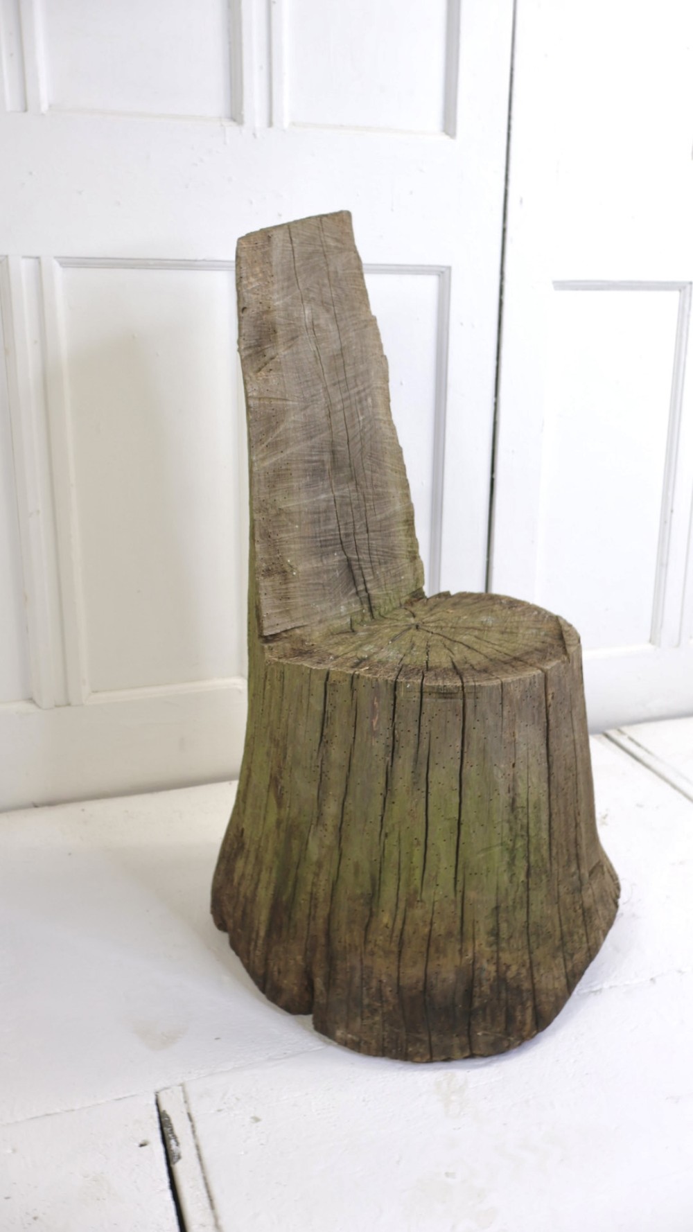 A rustic single-piece wooden seat carved directly from a weathered tree trunk with an upright backrest and natural grain splits.