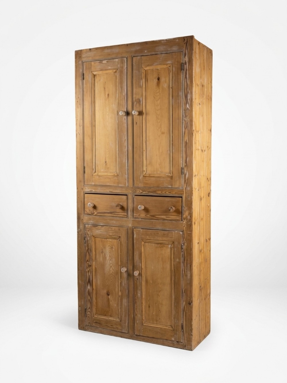 A tall 19th-century pine housekeeper cupboard featuring upper and lower panelled double doors and two central drawers.