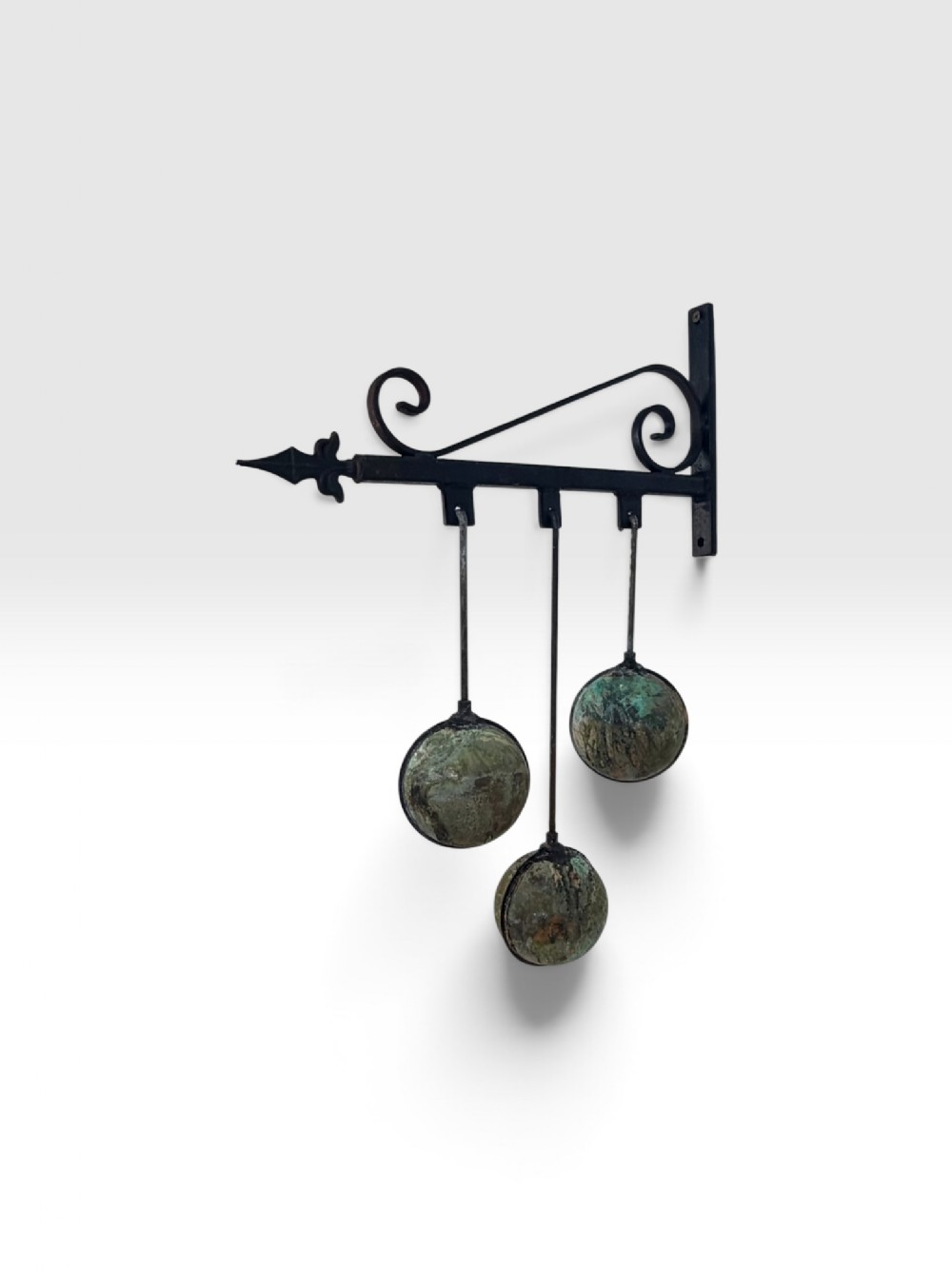 An early 20th-century wall-mounted wrought iron bracket with scrollwork supporting three suspended verdigris copper spheres.