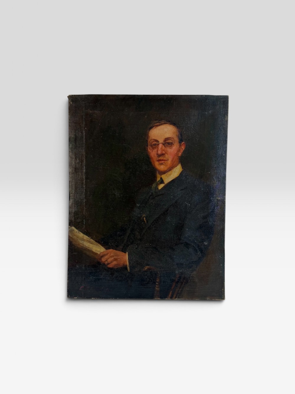 An unframed Edwardian oil painting on canvas depicting a seated gentleman wearing spectacles and a dark suit holding a paper.