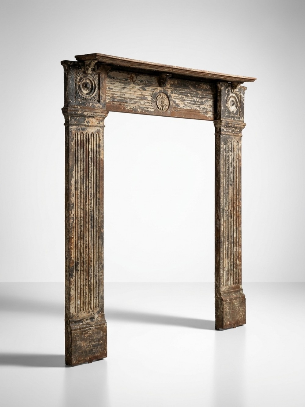An antique Georgian cast iron fire surround featuring fluted pilasters, rosette medallions, and a weathered patinated finish.