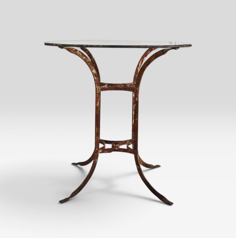 A nineteenth-century French wrought iron garden table featuring a circular clear glass top resting on a distressed red painted iron frame with sweeping curved legs.