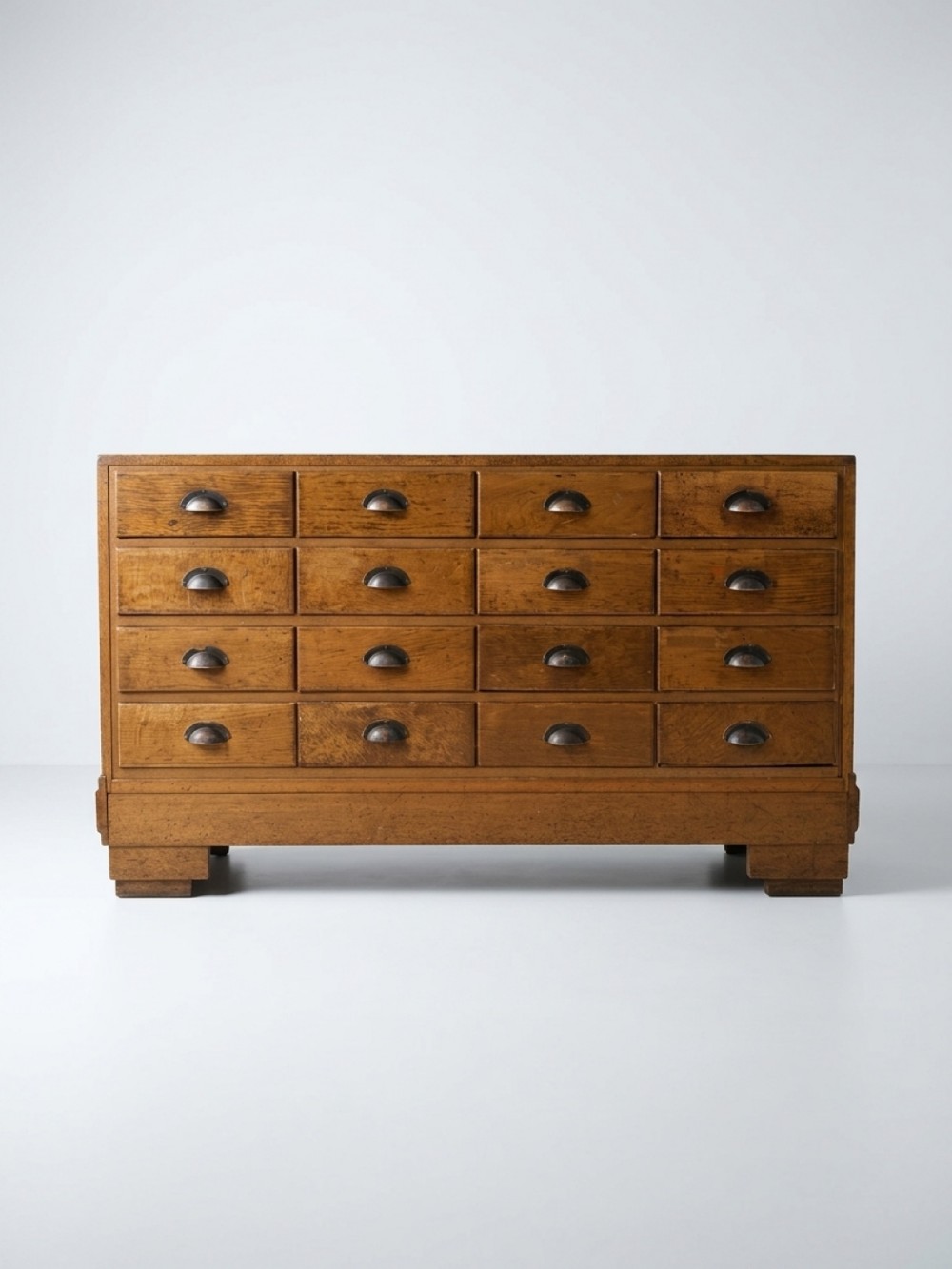 A 1920s oak haberdashery cabinet featuring sixteen drawers arranged in a four-by-four grid with dark metal cup handles.