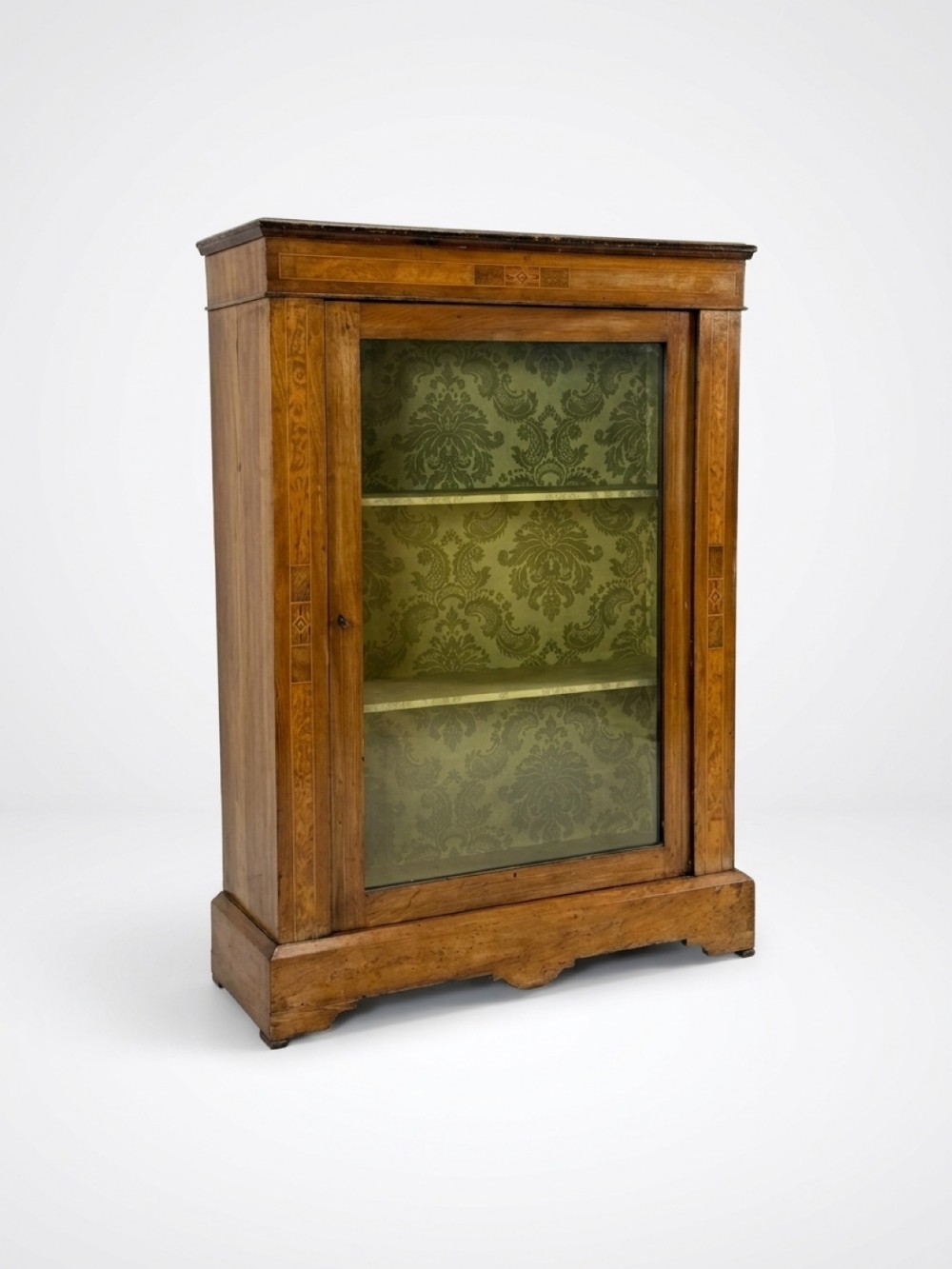 A 19th-century warm brown walnut pier cabinet featuring inlaid geometric borders, a single glazed door, and a green damask fabric-lined interior with shelves.